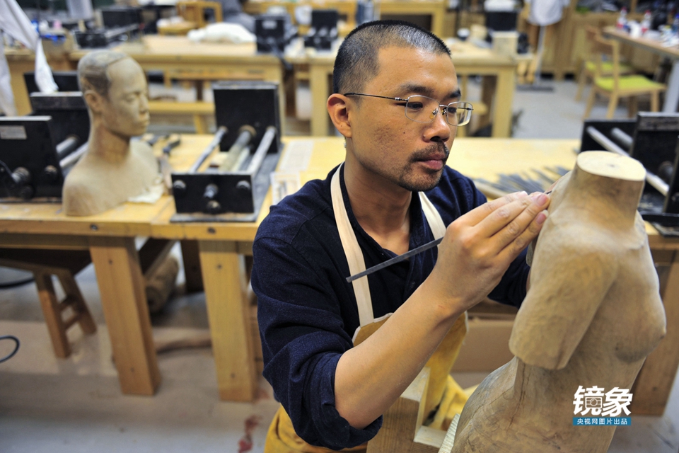 在清华大学美术学院雕塑系工作室,青年艺术家罗幻正在对一件木雕作品