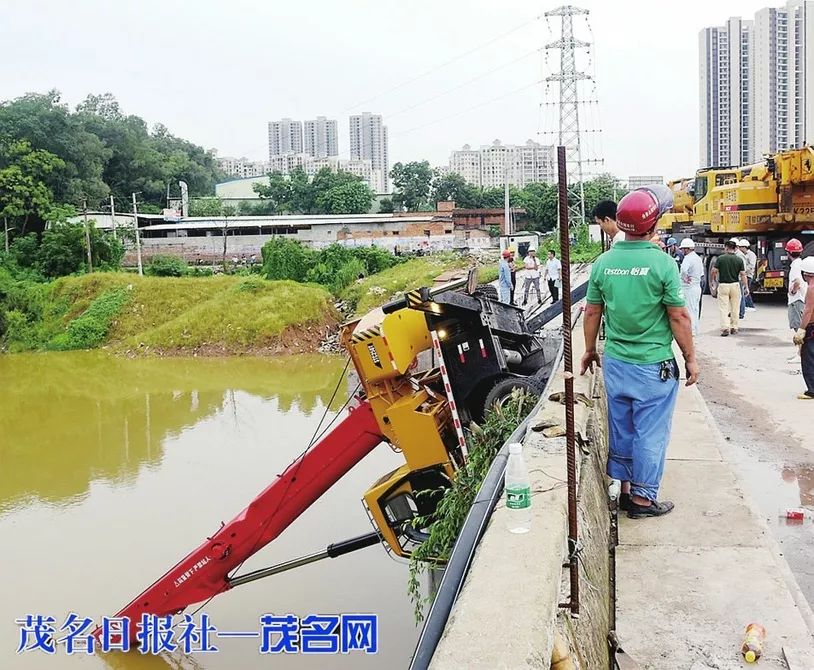 一辆黄色吊车侧翻在河里,部分吊臂已浸入水中,驾驶室刚好在河表面上