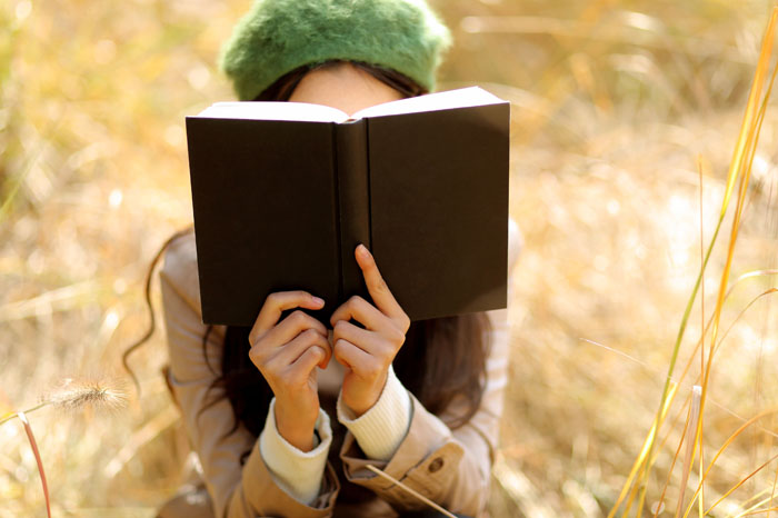 Woman covering face with book in autumn park